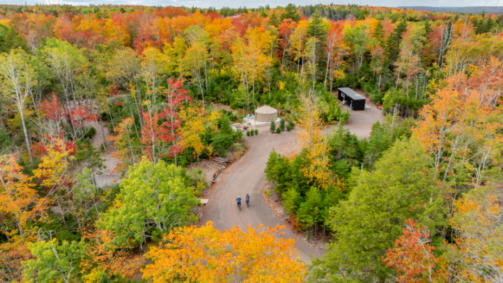 A drone view of a forest in the fall. There is a yurt accommodation in the view among leaves that have changed colours in the fall. Drone view of accommodations - Location: Seek Wilderness Accommodation, Truro, Bay of Fundy & Annapolis Valley